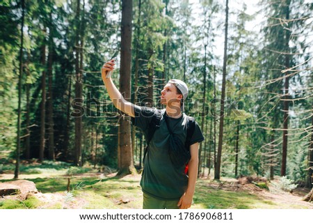 Young male tourist looking for a cellular network on a smartphone in a beautiful forest, lifted a phone up and looks at the screen with a serious face. Guy uses the Internet on a smartphone on a hike
