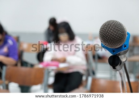 Close up of a stand microphone on the lecturer table inside college classroom with blure students as background. Education stock photo.