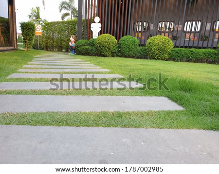 Walkway to the toilet is a large stone slab interspersed with green grass and has signs. Thai in pictures means no smoking