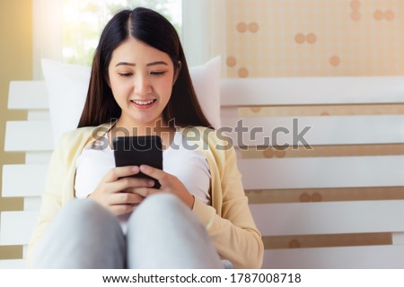 Happy young asian woman using mobile phone for online shopping, financial, transfer money, internet banking, searching information, chatting with friend, text messaging on bed at bedroom with smile