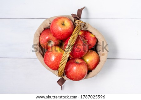 basket with ripe red social apples on white wooden background