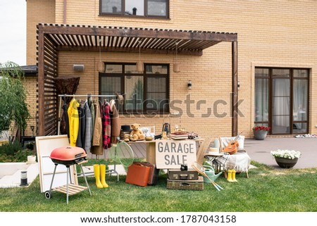 Garage sale sign placed at table with unique goods in backyard of beautiful brick house
