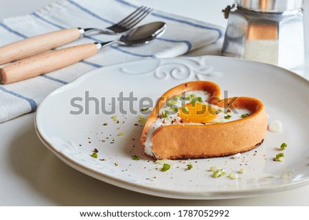 Heart shaped sausage with fried egg inside, on a plate with spoon and fork.