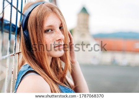 Portrait of beautiful ginger, teen girl listening to music, headphones on her head.