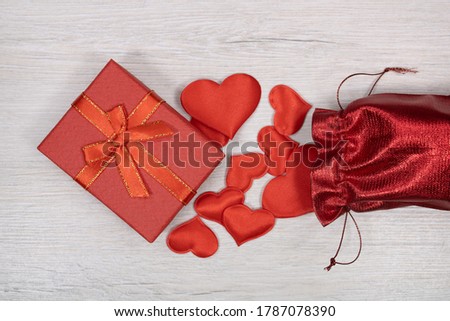 Red hearts pour out from a gift red bag. A gift in a box.