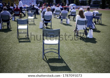 People sit on chairs apart one from another to maintain the social distance during the Covid-19 outbreak at an outdoor event on the turf of a stadium. Royalty-Free Stock Photo #1787095073