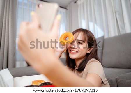 Young woman while watching TV, relaxing, eating snack and donut by ordering delivery,  at home on holiday.  junk food, unhealthy meal, obesity risk.