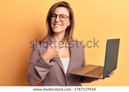 Young beautiful woman holding laptop smiling happy pointing with hand and finger 