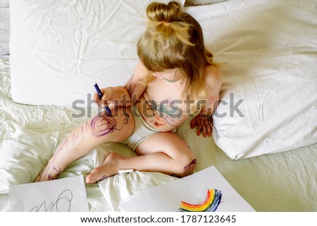 Cute baby draws with a marker on a white bed. smeared hands and feet, dirty in paint. Funny picture, funny kid.