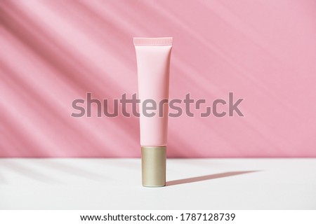 Pink tube of soft organic natural eye cream with golden cap on white pink background, palm leaf shadow. Summer facial product, sun lotion. Women's hygiene cosmetic accessory for skincare. Copy space. Royalty-Free Stock Photo #1787128739