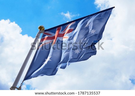 Large australian flag waving in the wind with a blue sky background