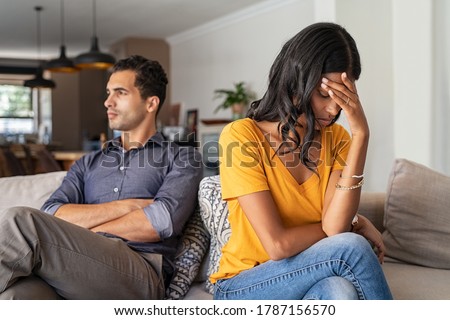 Middle eastern young couple sitting on couch after a fight. Sad indian woman sitting with hand on head after quarrel with boyfriend at home. Angry couple ignoring each other, relationship troubles. Royalty-Free Stock Photo #1787156570