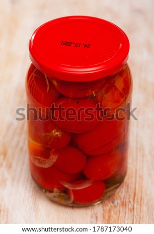 Glass jar of canned red tomatoes on wooden table, nobody