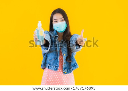 Portrait beautiful young asian woman wear mask for protect coronavirus or covid19 with alcohol gel for clean on yellow isolated background