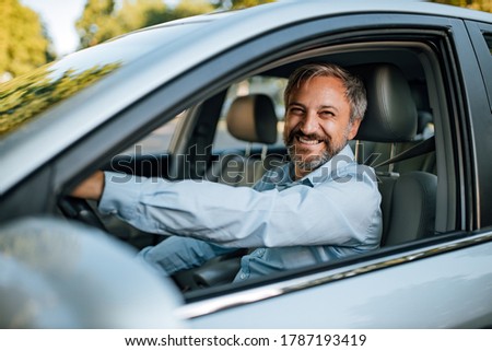 An older man smiling in the camera while he prepares to drive a car. Royalty-Free Stock Photo #1787193419