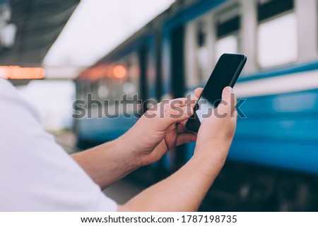 The guy holds a smartphone in his hands on the background of the train at the railway station