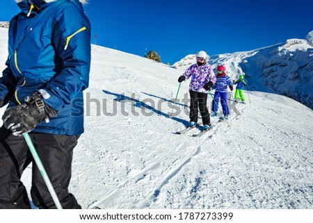 Three of kids ski on the Alpine slope as part of the school group one after another with mountains on background