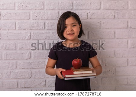 Back to school. Little girl holds books and an apple near a white brick wall. Child from elementary school. Education.