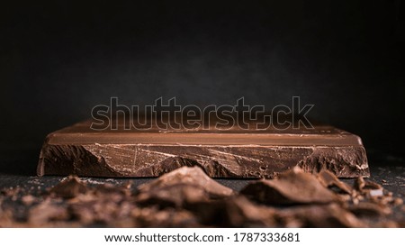 A cut of a large bar of dark chocolate on a black background banner. Macro, close-up on the texture with copy space.