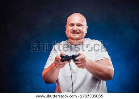 Plump gamer playing a game console with a great pleasure, standing on a blue contrasting background