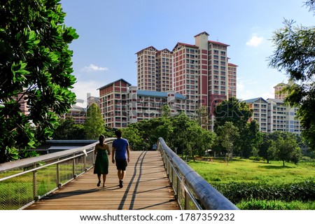 Couple enjoying afternoon walk in lush green neighbourhood park on bright sunny day. High rise public housing (HDB flats) in the background, Singapore Royalty-Free Stock Photo #1787359232