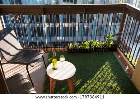 Apartment balcony in city with grass turf, potted plants and wine. Evening light. Royalty-Free Stock Photo #1787364911