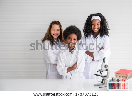 Group of multiracial friends with different types of skin together. Multi ethnic friend of happy child student wear white gown with stand arms crossed and smile with microscope and test tube in lab.