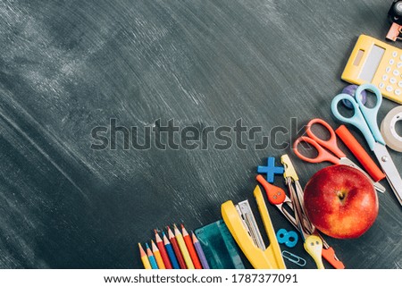 top view of ripe apple and school stationery on black chalkboard with copy space