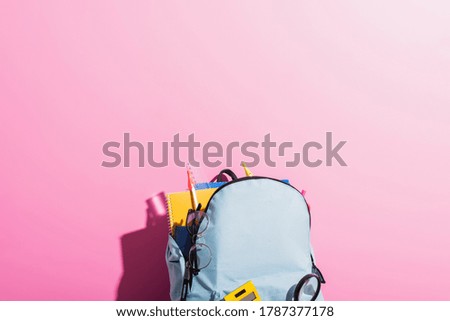 blue backpack with school stationery and eyeglasses on pink