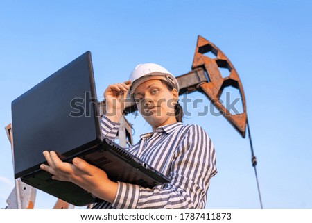 A female inspector with a laptop, in an oil field. Oil pumpers.
