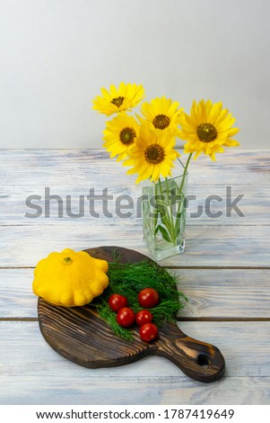 Still life of yellow flowers in glass vase and vegetables on wooden table. Cherry tomatoes, mini patty pan squashes, dill. Healthy food concept.