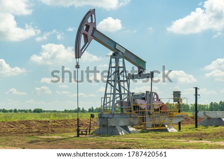 Oil pump in the field, beautiful blue sky with clouds. Russian oil production