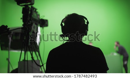 Film crew in green studio shooting video. Chroma - technology of combining two or more images or frames in single composition. Cameraman,director,crew. Filmmaking industry. Royalty-Free Stock Photo #1787482493