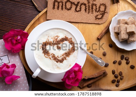 porcelain cup of coffee with ice cream and cinnamon heart served  at black wooden table with pink roses. life style concept