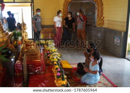 Blurred picture of a Buddhist to make merit in the temple with wearing mask and social distancing on the new normal concerned with after COVID-19 crisis in Thailand.