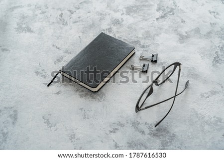 black diary, glasses and paper clips on the table