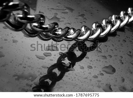 Black and white photograph of a chain on a black background with water drops
