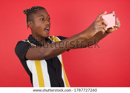 Close-up portrait African american man with braids wearing casual shirt over isolated red background taking a selfie to post it on social media or having a video call with friends. Royalty-Free Stock Photo #1787727260