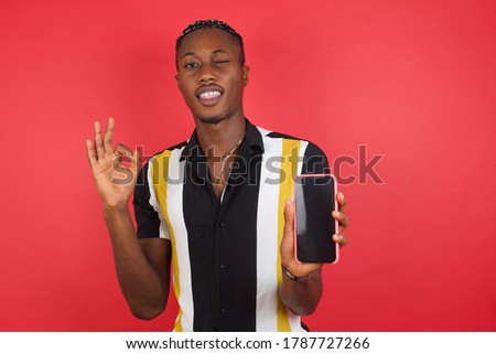 Portrait African american man with braids wearing casual shirt over isolated red background holding in hands cell showing ok-sign  Royalty-Free Stock Photo #1787727266