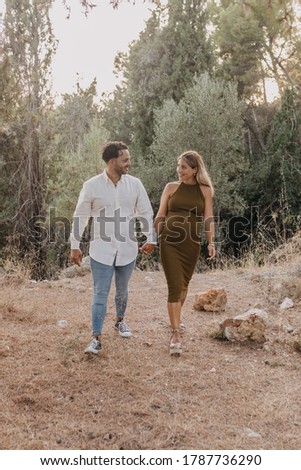 Pregnant couple walking in the woods. Pregnant blonde woman with her brunette boyfriend