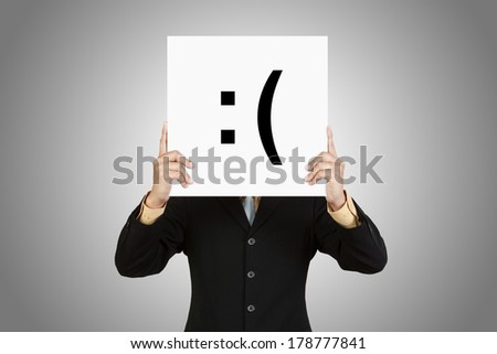 Businessman hold board with sad face emoticon on gray background