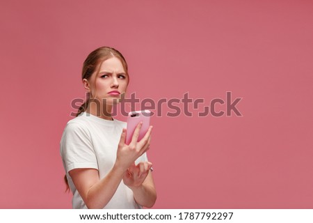 Confused young redhead woman holding pink smartphone.Embarassed woman has problem with broken not working mobile phone.Receiving bad news or email,spam message.Young people working with mobile devices.