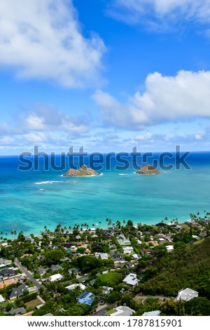 A photo from a mountain top in Oahu. Light blue ocean water seen in the distance and two small islands. Blue cloudy sky. High quality photo