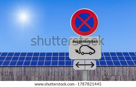 Traffic sign charging station for electric cars only in front of photovoltaics on wooden buildings against a blue sky with bright sun german language