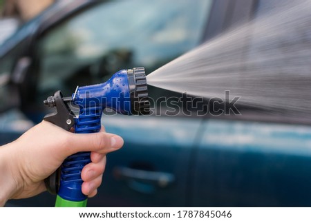 A woman's hand holds a hose for washing the car. Water, spray, jet. The idea is to wash your car in front of your house, saving after a pandemic. Photo close-up, horizontal