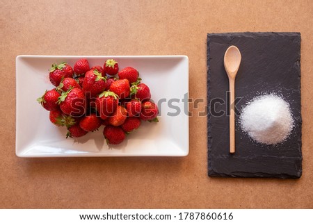 Forest fruits, strawberries and sugar on a white rectangular plate. on a brown base with shadows. wooden spoon. Whole strawberries on a plate.