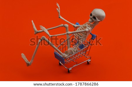 Halloween, scary theme. Skeleton and shopping trolley on orange background.