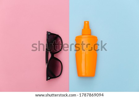 Beach vacation. Sunblock bottle and sunglasses on pink blue background. Top view. Flat lay