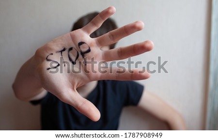 Teen boy defends himself with his palm on his hand written "Stop"