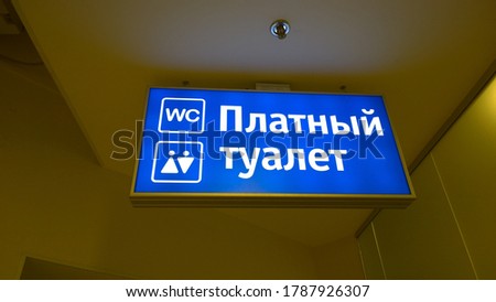 Blue backlit sign. Public WC. Text Translation from Russian: Paid toilet.